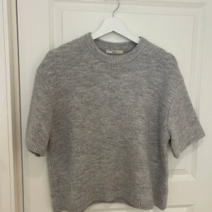 Grå stickad tröja från Gina Tricot - Säljer en mysig grå stickad tröja från Gina Tricot i premiumkvalitet. Tröjan har korta ärmar, perfekt för en molnig sommar dag. Enkel och stilren design som passar till det mesta. Nästan helt ny, knappt använd. Orginalpris 299kr