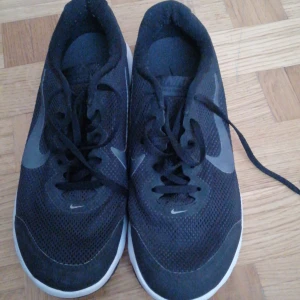 Svarta Nike sneakers - Säljer ett par svarta Nike sneakers med vit sula och snörning. Skorna har en stilren design med det klassiska Nike-loggan på sidan. Perfekta för en sportig look eller vardagsbruk.