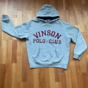 Grå hoodie från Vinson Polo Club - (LÄS ANNONS)!!!                                               Säljer en grå hoodie från Vinson Polo Club med röd vintage text på framsidan. Tröjan har en klassisk ficka och en bekväm huva. Perfekt för en avslappnad stil. Storleken är M men passar också S (Den är alltså lite mindre i storlek!)