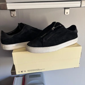  Axel Arigato zip - Snygga svarta sneakers från Axel Arigato med dragkedja. Skorna har en stilren design med vit sula och är tillverkade i mocka. Denna model tillverkas inte mer och därför är aningen mer sällsynta, arigato väska finns, påse finns, ordersbekräftelse finns direkt från axel arigato.