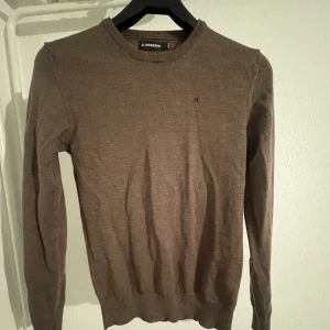Brun tröja från J.Lindeberg - Säljer en stilren brun tröja från J.Lindeberg. Tröjan har en klassisk rund hals och långa ärmar, perfekt för kyligare dagar. Den är tillverkad i ett mjukt material som ger en bekväm passform. Perfekt för dig som vill ha en tidlös look.