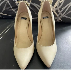 Högklackade pumps från Bertie 37 skinn - Eleganta beige pumps från Bertie med spetsig tå och klack. Skorna har en fin rosettdetalj baktill som ger en extra touch av stil. Perfekta för att lyfta vilken outfit som helst. Använda 1 gång. Mycket fint skick . Köpta i Köpenhamn 