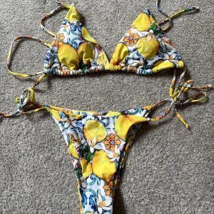 Färgglad bikini med citronmönster - Säljer en superfin bikini med citronmönster i härliga färger. Toppen har trekantsform och knytband, medan trosorna har knyt i sidorna. Perfekt för sommarens stranddagar! 🍋 passar kvinnor med medelstor byst. Använd en gång. 