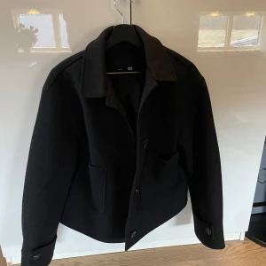 Svart kappa från 157 - Snygg svart kappa från 157 med klassisk krage och knappar framtill. Jackan har en stilren design med långa ärmar och fickor på sidorna.  Inte använd endast provad ❤️