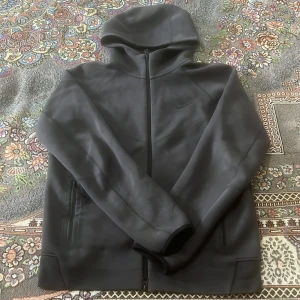 Svart hoodie från Nike - Säljer en stilren svart hoodie från Nike med dragkedja och huva. Perfekt för kyliga dagar. Den har långa ärmar och praktiska fickor med dragkedja.