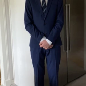 Blå kostym med vit skjorta - Snygg blå kostym med kavaj och matchande byxor. Kavajen har två knappar och klassiska slag. Den vita skjortan är långärmad med knappar framtill. Kostym endast använd 1 gång, nyskick. Nypris 2700kr (Dressman) Kavaj mörkblå Slim Fit  strl 44S Kostymbyxa mörkblå strl 30-30 Skjorta vit Slim Fit strl XS