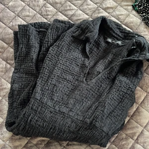 Svart klänning från Zara - Säljer en svart klänning från Zara med krage och långärmad design. Klänningen har en texturerad yta och en avslappnad passform. Perfekt för en stilren look.