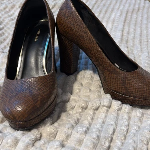 Bruna skor - Snygga bruna pumps med ormskinnsmönster från Attitude. De har en rund tå och en stabil klack som ger extra höjd. Perfekta för att ge din outfit en elegant touch.