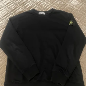 Svart tröja från Stone Island - Säljer en stilren svart tröja från Stone Island med deras ikoniska märke på ärmen. Tröjan har långa ärmar och en rund halsringning, perfekt för en casual look.