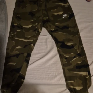 Grå mjukisbyxor från Nike bra skick på dem gröna nike byxorna - Säljer ett par grå mjukisbyxor från Nike med svarta detaljer och snörning i midjan. Byxorna har en dragkedja på sidan och är perfekta för en avslappnad stil.