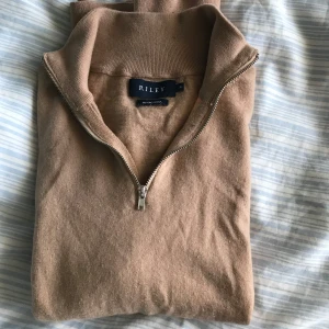Merino Ull tröja från Riley - Säljer en stilren beige tröja från Riley i mjuk merinoull. Tröjan har en praktisk dragkedja vid halsen och långa ärmar. Perfekt för kyligare dagar. Storlek M men passar Xs, bra skick behöver bara strykas.