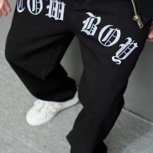 Svarta byxor med cowboy-tryck - Coola svarta byxor med stort vitt 'COWBOY' tryck på framsidan. Byxorna har en loose passform och är perfekta för en avslappnad stil. De är tillverkade i ett bekvämt material och har en dragkedja. Dom är också VÄLDIGT baggy vid benen