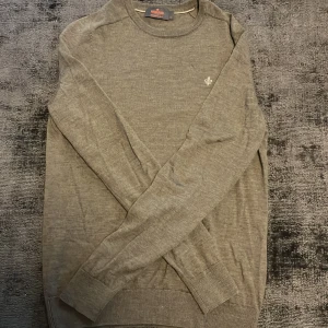 Brun grå  tröja från Morris - Säljer en stilren grå tröja från Morris i 100% merinoull. Tröjan har en liten broderad logga på bröstet och ribbade muddar vid ärmslut och nederkant. Priset är distribuerat 