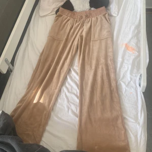 Beige mjukisbyxor från Juicy Couture - Säljer ett par beige mjukisbyxor från Juicy Couture. Byxorna har en loose passform med hög midja och snörning i midjan. De är tillverkade i ett mjukt material och har fickor både fram och bak med knappar.Har även bara använt de typ en gång o de passa inte riktigt eftersom jag är längre men de passar folk i 150cm kan diskutera.