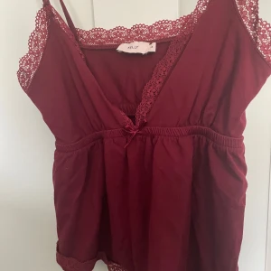 Vinröd topp Nelly - Säljer en söt vinröd linnetopp från Nelly med spetsdetaljer och smala axelband. Toppen har en v-ringad design och en liten rosett framtill. Perfekt för en somrig look! Storlek XS, använd fåtal gånger men som ny 