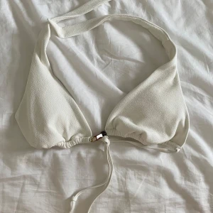 Vit bikiniöverdel med knytband - Snygg vit boho bikiniöverdel med knytband i nacken och ryggen. Den har dekorativa pärlor i brunt och guld vid knytningen framtill. Använd högst 2 gånger, säljer då den var för liten på mig 🥹🩷