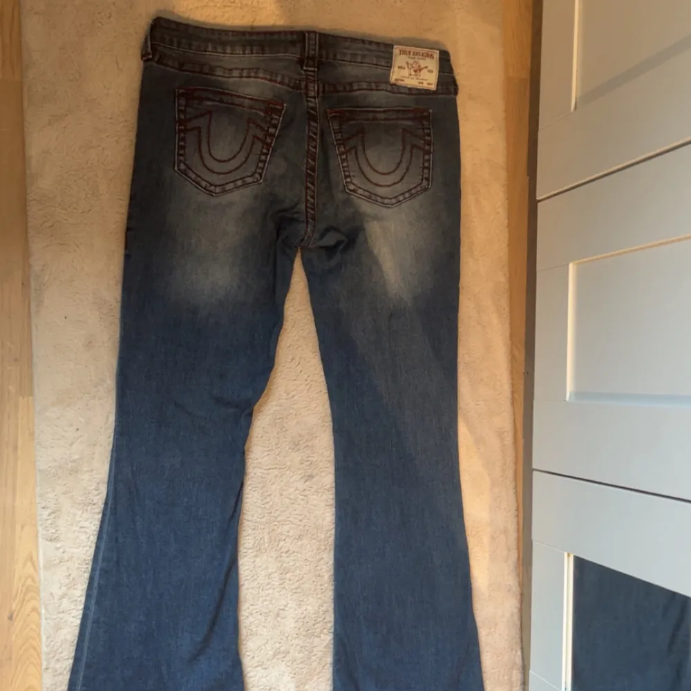 Snygga blå jeans från True Religion med klassisk femficksdesign och kontrastsömmar i rött. De har en bootcut-stil och är perfekta för en avslappnad look. Märkeslogga på bakfickan ger en extra touch. Använda 2 gånger.. Farkut & Housut.