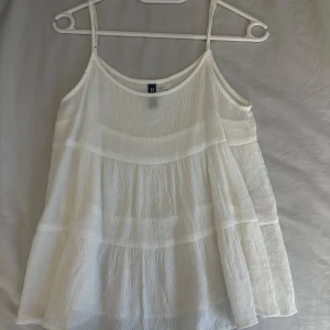 Vit ärmlös linnetopp - Säljer en luftig och stilren vit linnetopp med tunna axelband. Toppen har en lätt och flödande design som passar perfekt för varma dagar. Perfekt att matcha med jeans eller shorts för en avslappnad look.