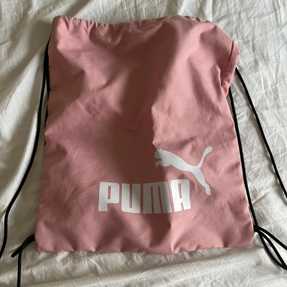 Säljer en snygg rosa gympapåse från Puma med svart dragsko. Perfekt för träning eller som en lätt ryggsäck. Den har en stor Puma-logga i vitt på framsidan. Enkel och stilren design som passar till mycket.. Laukut & Käsilaukut.