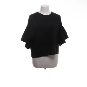 Svart blus från Zara Woman - Snygg svart blus från Zara Woman med korta ärmar och volangdetaljer. Perfekt för en stilren look. Blusen har en rund halsringning och en liten öppning bak i nacken.