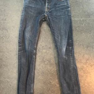 Blå jeans från Nudie Jeans - Snygga blå jeans från Nudie Jeans med klassisk femficksdesign och orange sömmar. De har en ”Slim” passform och är tillverkade i slitstarkt denim. Perfekta för en avslappnad stil. Jag säljer dessa eftersom att dom inte passade mig, dom är aldrig använda. Priset är inte hugget i sten så kom gärna med prisförslag.