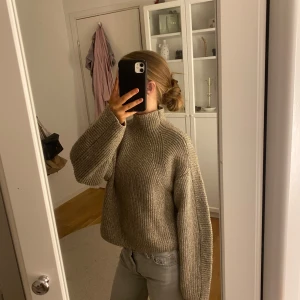 Beige stickad tröja från H&M - Säljer en mysig beige stickad tröja från H&M. Tröjan har en hög krage och långa ärmar, perfekt för kyligare dagar. Den har en ribbad struktur som ger en stilren look. Passar bra till jeans eller kjol för en avslappnad stil.