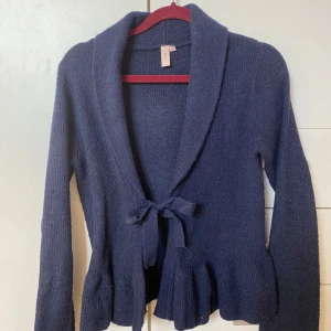 Mörkblå stickad kofta från Nelly - Säljer en mysig mörkblå stickad kofta från Nelly. Koftan har långa ärmar och en knytning framtill som ger en fin detalj. Perfekt för kyliga dagar. 💙