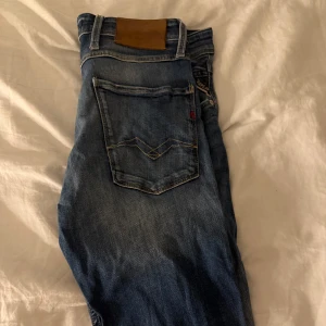Blå jeans från Replay - Snygga blå jeans från Replay i modellen Anbass. De har en slim fit passform och klassisk femficksdesign med dragkedja. Perfekta för en stilren look. Jag säljer dom för dom är för små för mig. 