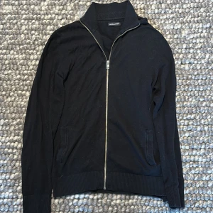 Svart fullzip från Jack & Jones - Snygg svart tröja från Jack & Jones med dragkedja framtill. Perfekt för en stilren look. Tröjan har långa ärmar och ribbade detaljer vid ärmslut och nederkant.