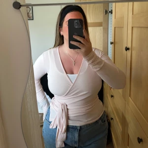 Ljusrosa omlottopp - Säljer en ljusrosa omlottopp med långa ärmar och knytband i midjan. Toppen har en v-ringad design och är perfekt för en stilren look.