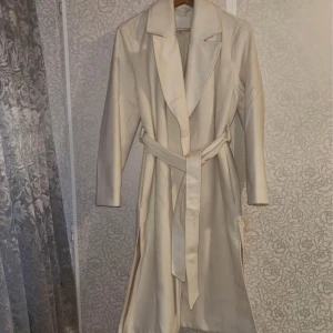 Kappa  - Elegant beige trenchcoat med knytbälte i midjan. Jackan har en klassisk krage och långa ärmar, perfekt för en stilren look. Är i storlek 32 men passar även 34. Har använts en gång. 