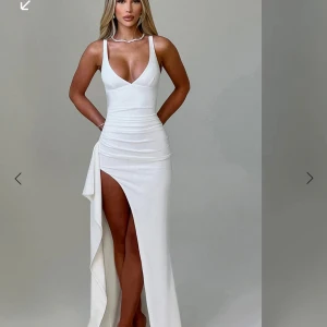 Vit långklänning med slits från BABYBOO  - Elegant vit långklänning med djup v-ringning och hög slits. Klänningen har smala axelband och en figurnära passform som framhäver silhuetten. Perfekt för en glamorös kväll. 