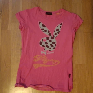 Rosa t-shirt från Playboy - Säljer en rosa t-shirt från Playboy. T-shirten har ett  tryck av den ikoniska kaninen i ett mönster på framsidan och texten 'Playboy'på både fram och baksidan.