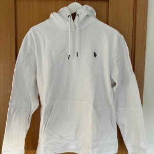 Vit Ralph lauren hoodie - Säljer en stilren vit Polo Ralph Lauren assn hoodie med en liten broderad logga på bröstet. Tröjan har en klassisk känguruficka och justerbar huva med snören. Perfekt för en avslappnad look.