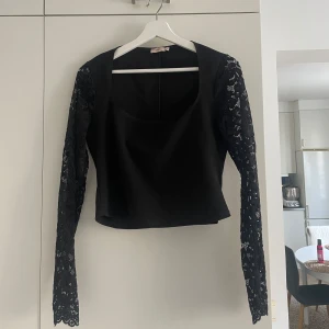 Svart topp med spetsärmar från Nelly - Elegant svart topp från Nelly med långa spetsärmar. Perfekt för en kväll ute eller en speciell tillställning. Toppen har en klassisk passform och en rundad halsringning🌸.