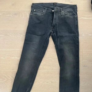 Gråmelerade Lee jeansbyxor - Snygga gråmelerade jeansbyxor från Lee med en klassisk femficksdesign. De har en knappgylf och är i en mörk tvätt som ger en stilren look. Perfekta för en avslappnad stil. W31 L 32. Rök och djurfritt hem.