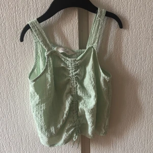 Mintgrön linnetopp från H&M - Säljer en söt mintgrön linnetopp från H&M med knytning framtill. Toppen har breda axelband och en luftig passform, perfekt för varma dagar. Passar bra till både jeans och kjol. 🌿