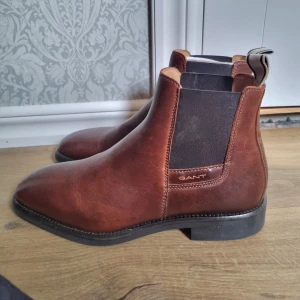 Bruna Chelsea boots från Gant - Snygga bruna Chelsea boots från Gant i skinn. De har en klassisk design med elastiska paneler på sidorna för enkel på- och avtagning. Nya I kartong