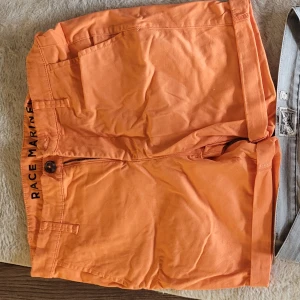 Orange shorts från Race Marine och grå jeansshorts - Säljer ett par orange shorts från Race Marine med knapp och dragkedja, samt ett par grå jeansshorts med klassisk femficksdesign.