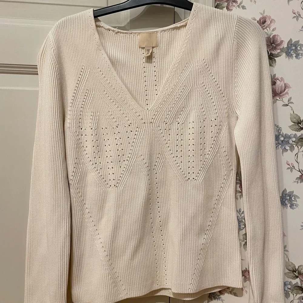 Säljer en stilren vit ribbad tröja från H&M med v-ringning och dekorativa stickade detaljer framtill. Tröjan har långa ärmar och en bekväm passform. Perfekt för en elegant och avslappnad look. Köptes förra sommaren, men den var för stor så den är inte använd.. Neuletakit & Villapaidat.