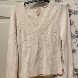 Vit ribbad tröja från H&M - Säljer en stilren vit ribbad tröja från H&M med v-ringning och dekorativa stickade detaljer framtill. Tröjan har långa ärmar och en bekväm passform. Perfekt för en elegant och avslappnad look. Köptes förra sommaren, men den var för stor så den är inte använd.