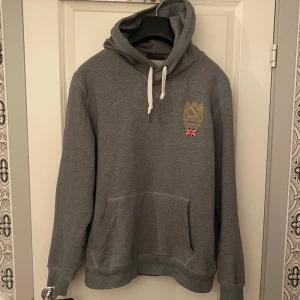 Grå hoodie från Morris - Säljer en snygg grå hoodie från Morris med broderad logga och brittisk flagga på bröstet. Modellen är 184cm lång och väger ca 75kg. Vid minsta fråga eller fundering hör av er.