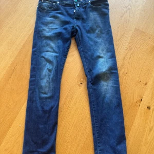  JACOB COHEN - Snygga blå jeans från Jacob Cohen med knappgylf och klassisk femficksdesign. Jeansen har en stilren look med en liten logga på baksidan. Perfekta för en avslappnad stil. Dessa sitter som 32 ish. 
