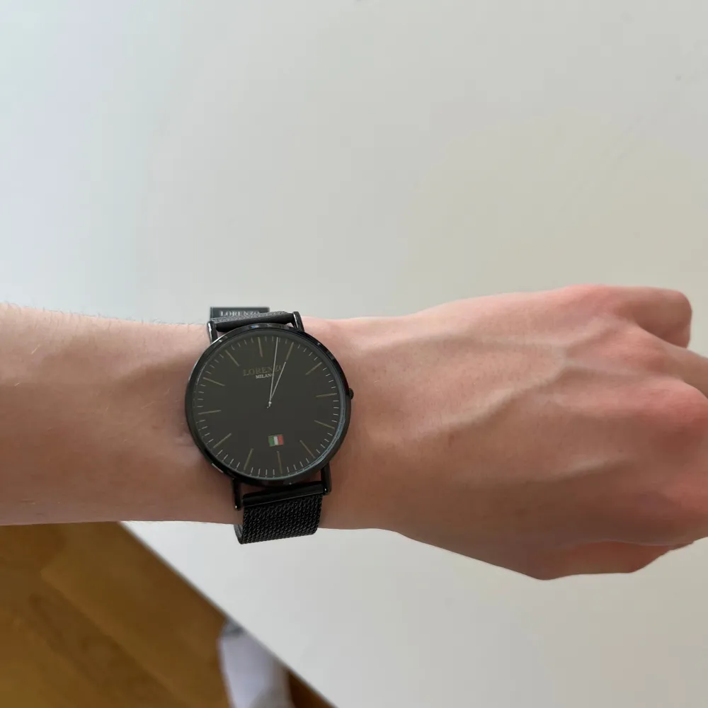 Stilren svart klocka från Lorenzo Milano med en minimalistisk urtavla och italiensk flagga. Klockan har ett svart mesh-armband som ger en modern look. Perfekt för dig som gillar enkel och elegant design.. Asusteet.