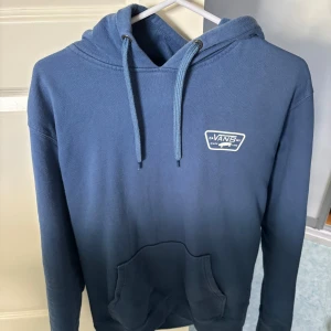 Blå hoodie från Vans - Säljer en snygg blå hoodie från Vans med logga på bröstet och ryggen. Tröjan har en klassisk känguruficka och justerbar huva med dragsko. Perfekt för en avslappnad stil!