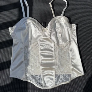 Vit korsett från H&M Divided - Snygg vit korsett från H&M Divided i satin med spetsdetaljer. Den har justerbara axelband och en elegant design som passar perfekt för speciella tillfällen.