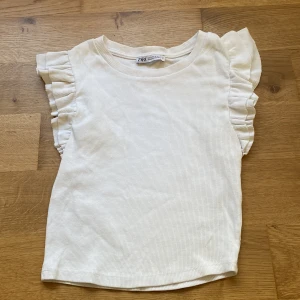 Jättefin ribbad topp från Zara.  - Säljer en söt vit ribbad topp från Zara med volangdetaljer på ärmarna. Toppen är ärmlös och har en rund halsringning. Köpte den på Zara. Storlek S