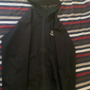 Svart vindjacka från Haglöfs - Säljer en svart vindjacka från Haglöfs i storlek M. Jackan har en dragkedja framtill och en justerbar huva. Perfekt för blåsiga dagar och utomhusaktiviteter.