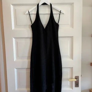 Svart glittrig klänning - Glittriga detaljer, halterneck och asymmetrisk nedtill. Köpt vintage