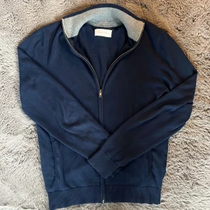 Marinblå fullzip från Pier One - Snygg marinblå fullzip från Pier One med dragkedja framtill och ribbade muddar. Perfekt för lager-på-lager och enkel att matcha. Skick 8/10. Säljer på grund av att den sällan används. Hör gärna av er om ni har några funderingar eller vill diskutera pris🤝